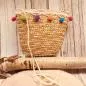 Preview: Kleine runde Korbtasche für Kinder aus naturfarbenem Rattan mit bunten Bommeln und Stoff-Innenfutter.