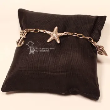Versilbertes Bettelarmband aus Metall mit großen Gliedern auf einem braunen Schmuckkissen präsentiert.