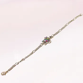 Ausgebreitetes versilbertes Bettelarmband aus Metall mit mittig platzierter Schildkröte und bunten Perlen auf hellem Untergrund.