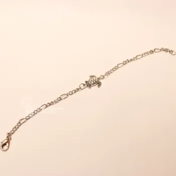 Ausgebreitetes versilbertes Bettelarmband aus Metall mit mittig platzierter Schildkröte vor hellem Hintergrund.