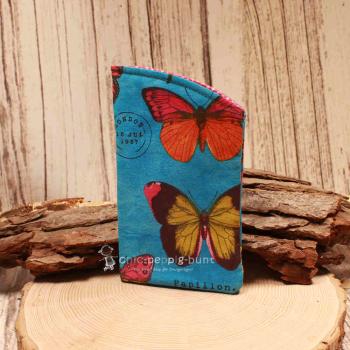 Handgenähtes Brillenetui von chic-peppig-bunt in Blau mit Schmetterlings-Motiv und pink-weiß gepunktetem Blumen-Innenstoff auf hellem Hintergrund.