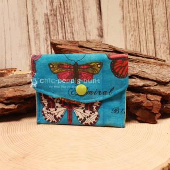 Kleiner handgenähter Geldbeutel von chic-peppig-bunt aus blauem Stoff mit Schmetterlingen und weiß-grün gepunktetem Futter auf hellem Hintergrund.