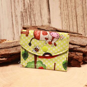 Kleiner handgenähter Geldbeutel von chic-peppig-bunt aus grünem Stoff mit Kuh-Motiv und gepunktetem Innenfutter auf hellem Hintergrund.