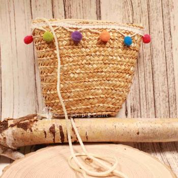 Kleine runde Korbtasche für Kinder aus naturfarbenem Rattan mit bunten Bommeln und Stoff-Innenfutter.