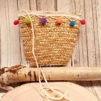 Kleine runde Korbtasche für Kinder aus naturfarbenem Rattan mit bunten Bommeln und Stoff-Innenfutter.