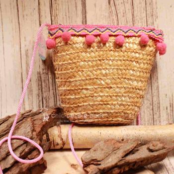 Kleine runde Korbtasche für Kinder aus naturfarbenem Rattan mit rosa Bommeln und Stoff-Innenfutter.