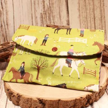 Großer handgenähter Geldbeutel von chic-peppig-bunt aus grünem Stoff mit Reiterin und Pferden sowie braun-weiß kariertem Futter auf hellem Hintergrund.