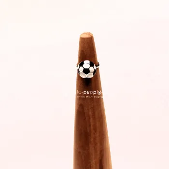 Verstellbarer Kinderring aus Metall mit schwarz-weißem Fußball-Motiv auf einem hölzernen Ringständer.