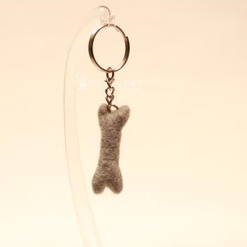 Handgefertigter Mini Knochen aus grauem Filz als witziger Schlüsselanhänger und weicher Taschenbaumler, Gesamtansicht.