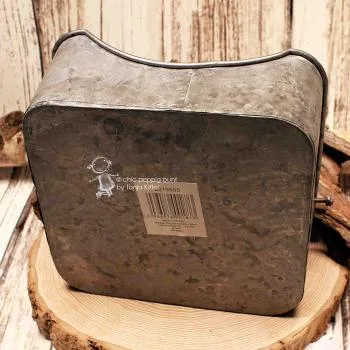 Unterseite des fleckigen Blech-Serviettenhalters mit Barcode-Aufkleber auf einer Holz-Baumscheibe.