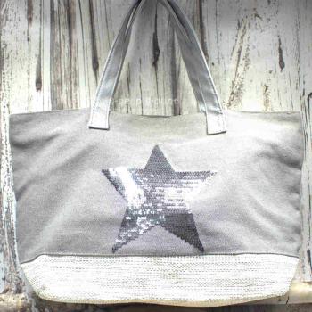 Große graue Shoppertasche mit silbernem Pailletten-Stern, weißem Boden-Element und grauen Kunstleder-Tragegriffen vor rustikalem Holzhintergrund.