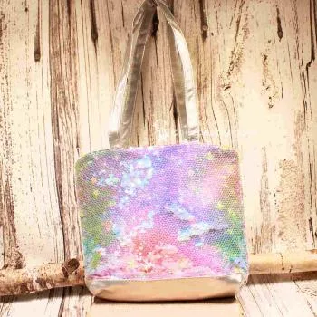 Kleine lila-blau schimmernde Kindertasche mit Pailletten-Stickerei, silbernem Boden und grauen Kunstleder-Griffen auf rustikalem Holzgrund.