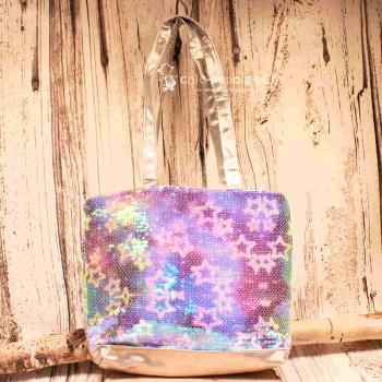 Kleine lila-blau schimmernde Kindertasche mit Sternen-Pailletten, grauen Kunstleder-Griffen und Reißverschluss auf hellem Untergrund.