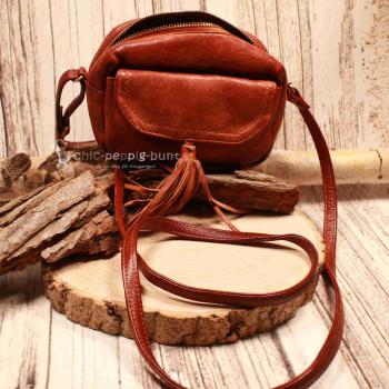 Kleine braune Umhängetasche aus Leder mit zwei dekorativen Quasten am Magnetverschluss und verstellbarem Schulterriemen.