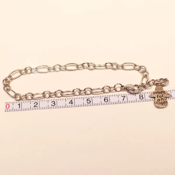 Versilbertes Bettelarmband an einem Maßband zur Veranschaulichung der Länge von 20 cm und 22 cm mit Engel.