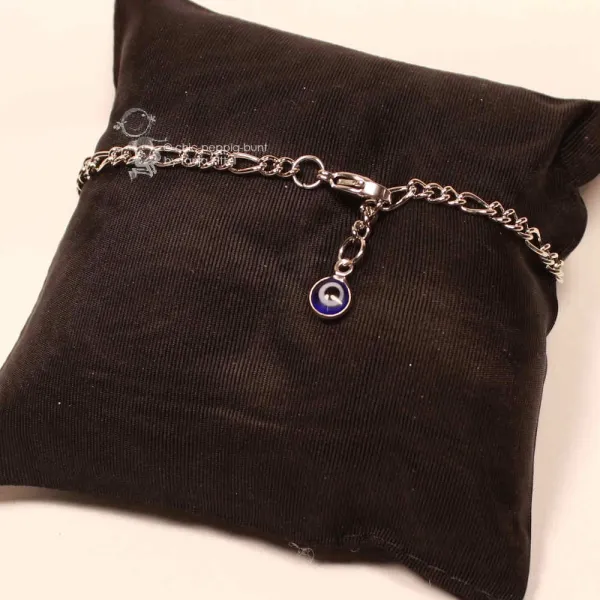 Versilbertes Gliederarmband mit blauem Auge-Anhänger präsentiert auf einem edlen schwarzen Schmuckkissen.