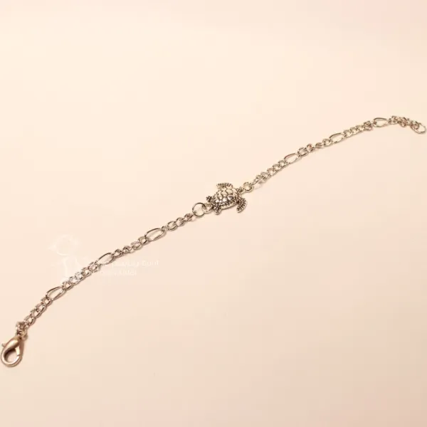 Ausgebreitetes versilbertes Bettelarmband aus Metall mit mittig platzierter Schildkröte vor hellem Hintergrund.