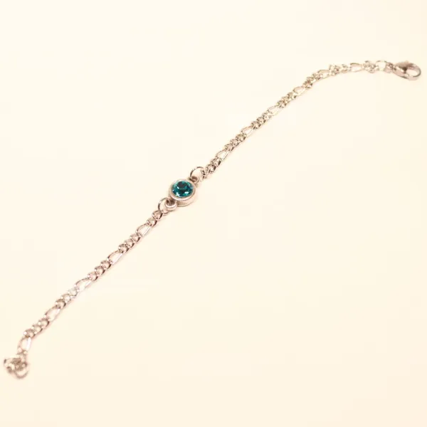 Ausgebreitetes versilbertes Bettelarmband aus Metall mit mittigem türkisblauem Swarovski Stein auf hellem Untergrund