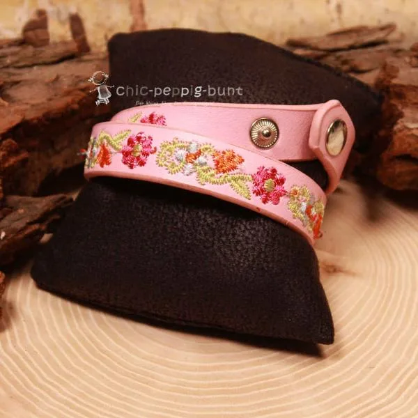 Nahaufnahme der farbenfrohen Blumen-Stickerei auf dem rosa Wickelarmband.