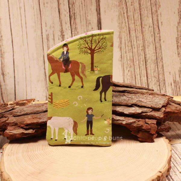 Handgenähtes grünes Brillenetui von chic-peppig-bunt mit Pferden und Reiterinnen sowie rosa-pink gepunktetem Innenstoff auf hellem Hintergrund.