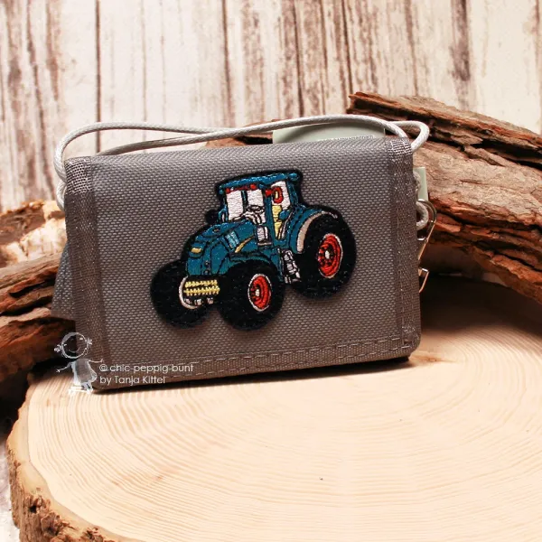 Grauer Kinder-Brustbeutel aus robustem Spinnstoff mit gesticktem, blau-schwarzem Traktor-Motiv und roten Felgen.