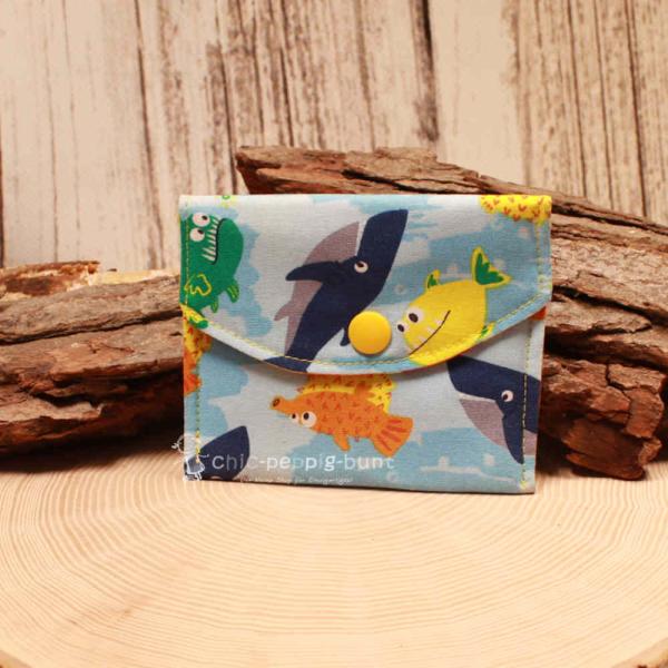 Kleiner handgenähter Geldbeutel von chic-peppig-bunt aus blauem Stoff mit Fisch-Motiv und bunt gestreiftem Innenfutter auf hellem Hintergrund.