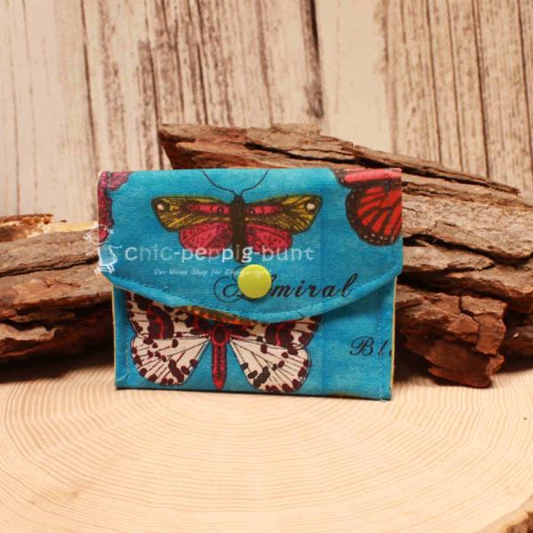 Kleiner handgenähter Geldbeutel von chic-peppig-bunt aus blauem Stoff mit Schmetterlingen und weiß-grün gepunktetem Futter auf hellem Hintergrund.