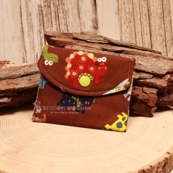 Kleiner handgenähter Geldbeutel von chic-peppig-bunt aus braunem Stoff mit Dinosaurier-Motiv und grün gepunktetem Innenfutter auf hellem Hintergrund.
