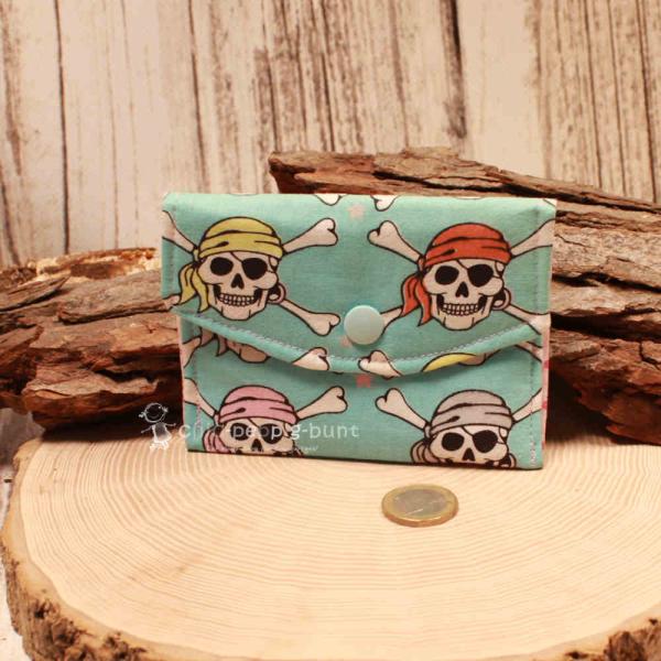 Kleiner handgenähter Geldbeutel von chic-peppig-bunt aus blauem Stoff mit Totenköpfen und rosa gepunktetem Innenfutter auf hellem Hintergrund.