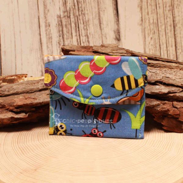 Kleiner handgenähter Geldbeutel von chic-peppig-bunt aus blauem Stoff mit bunten Insekten und grünem Punkt-Futter auf hellem Hintergrund.