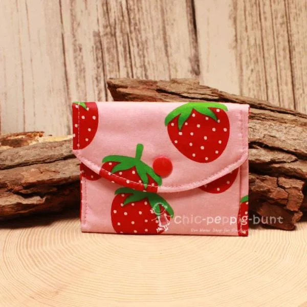 Kleiner handgenähter Geldbeutel von chic-peppig-bunt aus rosa Stoff mit Erdbeeren und rot-weiß gepunktetem Innenfutter auf hellem Hintergrund.