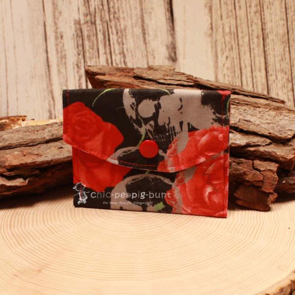 Kleiner handgenähter Geldbeutel von chic-peppig-bunt aus schwarzem Stoff mit roten Blumen und rot-weiß kariertem Futter auf hellem Hintergrund.