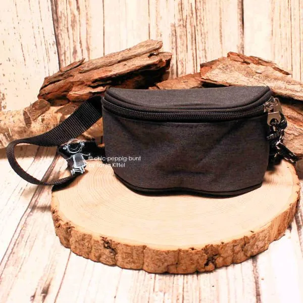Vorderansicht der kleinen schwarzen Stoff-Gürteltasche für Kinder auf einer rustikalen Holzscheibe präsentiert.