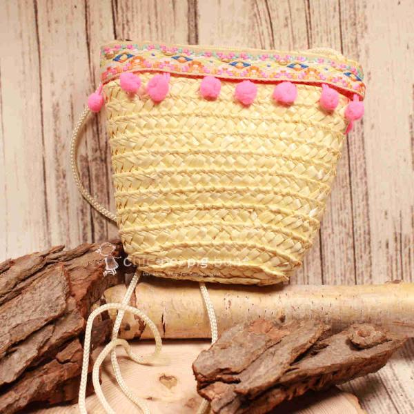 Kleine runde Korbtasche für Kinder aus naturfarbenem Rattan mit rosa Bommeln, heller Bordüre und Stoff-Innenfutter.