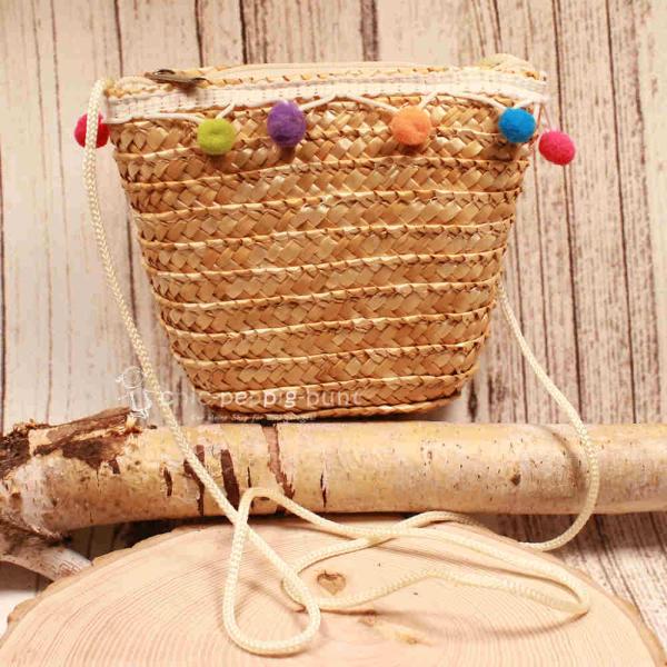 Kleine runde Korbtasche für Kinder aus natürlichem Rattan mit bunten Bommeln und Kordel-Schulterband.