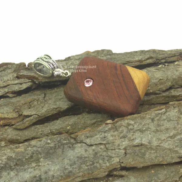 Handgeschliffener Holz Kettenanhänger aus zweifarbig verleimtem Holz mit eingearbeitetem Strass-Stein und versilberter Schluppe auf Baumrinde.