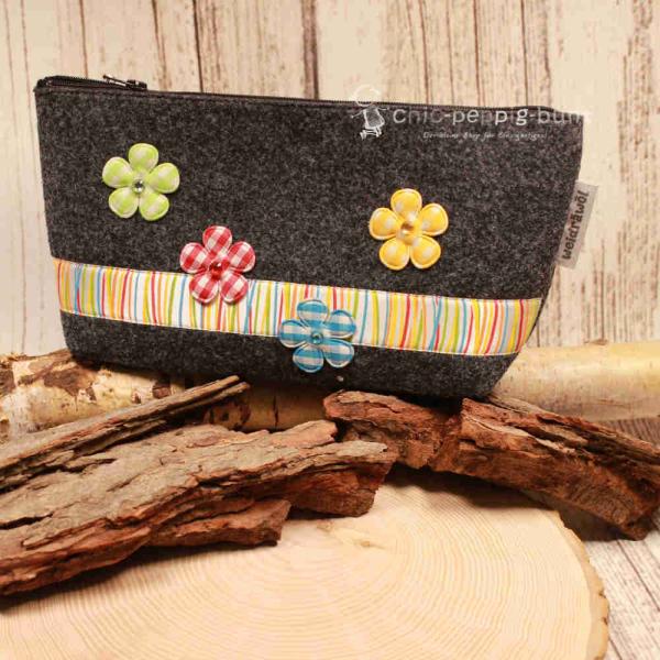 Handgenähte Kosmetiktasche aus dunkelgrauem Filz mit bunten Blumen und gestreiftem Band.