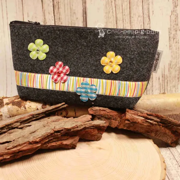 Handgenähte Kosmetiktasche aus dunkelgrauem Filz mit bunten Blumen und gestreiftem Band.