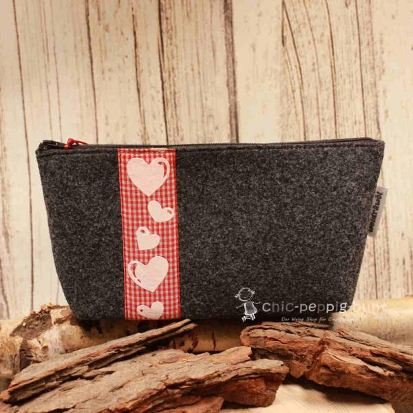 Handgenähte weidräwöl Kosmetiktasche aus grauem Filz mit Herz-Motiv und roter Karo-Bordüre.