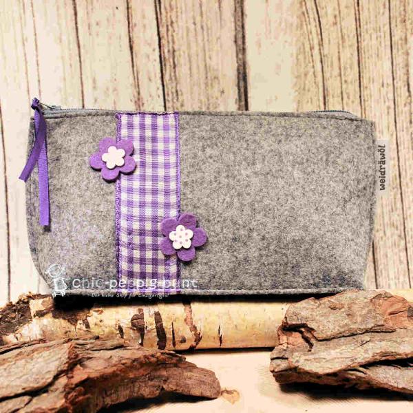 Handgenähte weidräwöl Kosmetiktasche aus hellgrauem Filz mit Blumen und lila Karoband.