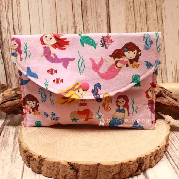 Großer handgenähter Geldbeutel von chic-peppig-bunt aus rosa Stoff mit Meerjungfrauen und pink gepunktetem Innenfutter auf hellem Hintergrund.