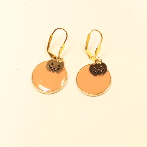 Vergoldete Ohrringe mit großem orangefarbenem Kürbis und kleinem goldenem Gesicht als Hänger für Halloween.