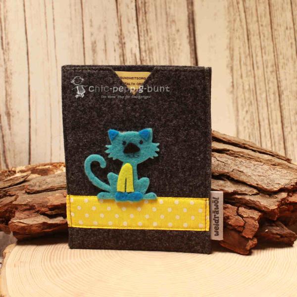 Handgenähte dunkelgraue Filz Passhülle der Marke Weidräwöl mit blauer Katzen-Applikation und gelber Bordüre mit weißen Punkten.