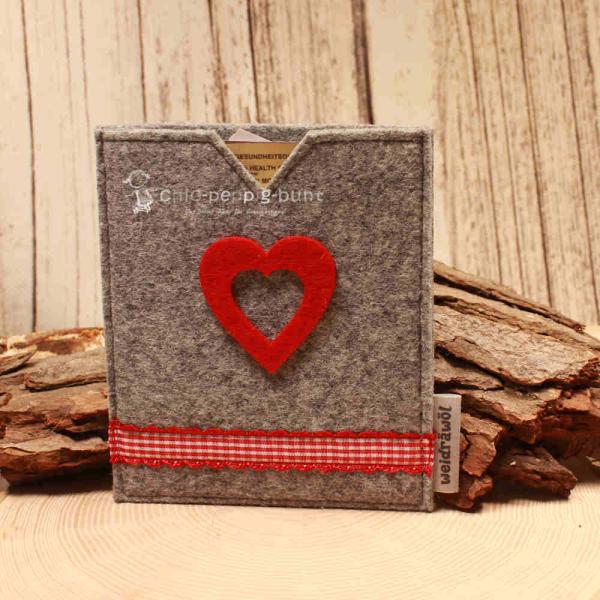 Handgenähte hellgraue Filz Passhülle der Marke Weidräwöl mit rotem Filzherz und rot-weiß karierter Bordüre für Reisepass und Impfpass.