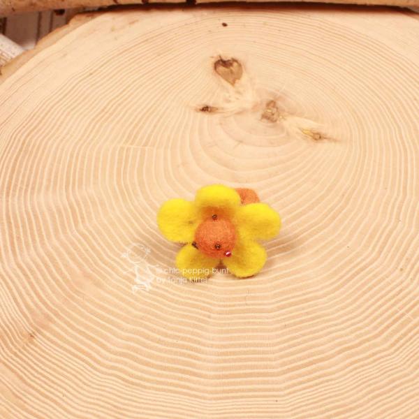 Handgefertigter gelber Filzring für Kinder in Blumenform mit orangefarbenen Akzenten auf verstellbarer Ringschiene.