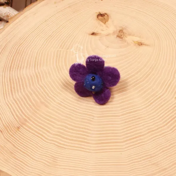 Handgefertigter lila-blauer Filzring für Kinder in Blumenform mit bunt bestickter Perlenmitte auf verstellbarer Schiene.