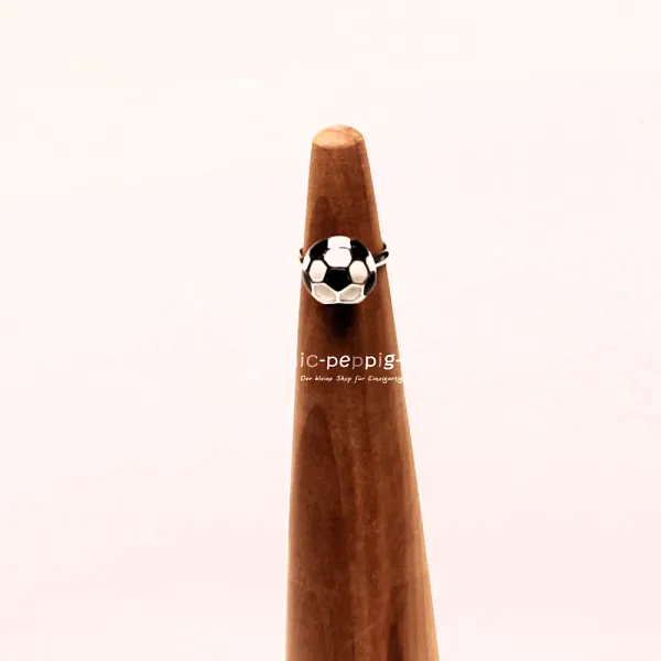 Verstellbarer Kinderring aus Metall mit schwarz-weißem Fußball-Motiv auf einem hölzernen Ringständer.