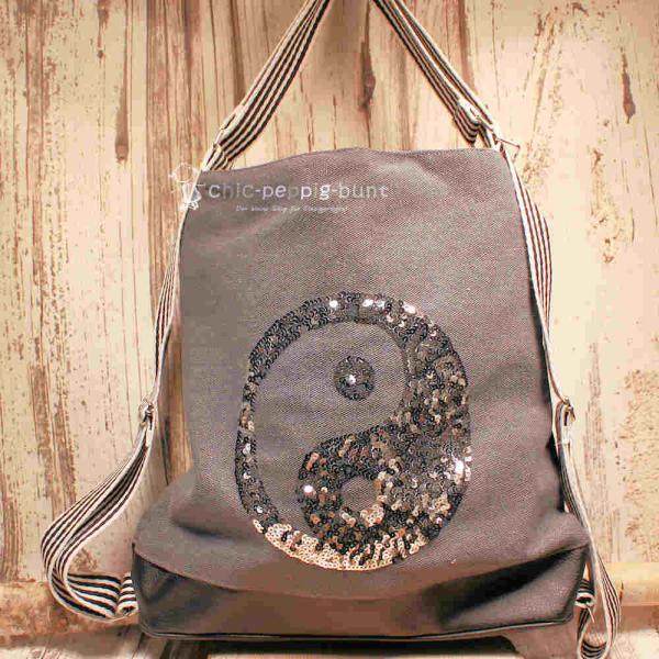 Grauer Rucksack aus Stoff mit silbernem Ying & Yang Symbol aus Pailletten, Lederboden und gestreiften Gurten, 3-in-1 Funktion als Handtasche.