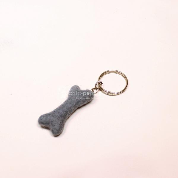 Handgefertigter Mini Knochen aus blauem Filz als witziger Schlüsselanhänger und weicher Taschenbaumler, hängend und liegend dargestellt.