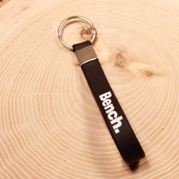 Schwarzer Bench Schlüsselanhänger aus Kautschuk mit weißem Schriftzug und silbernem Metallring.